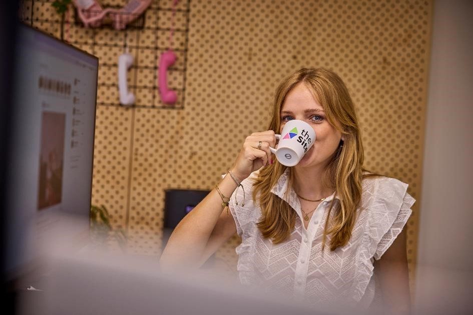 Iris van der Heijden met een mok van The Sitekick achter haar werkplek